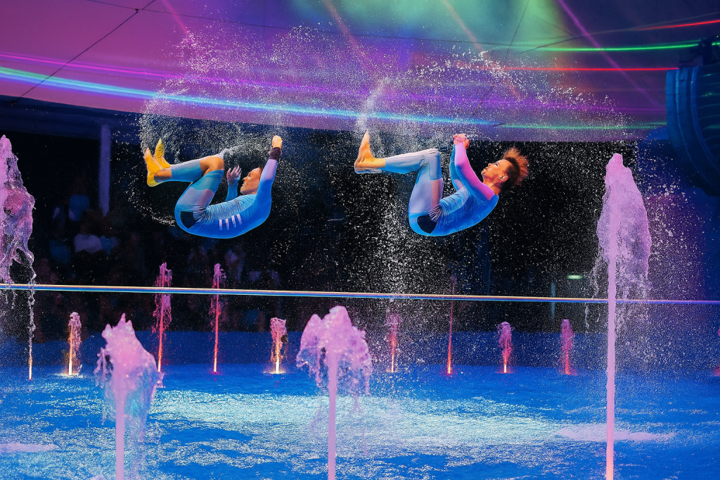 Aerial acrobats performing over a pool on a large cruise ship entertainment deck